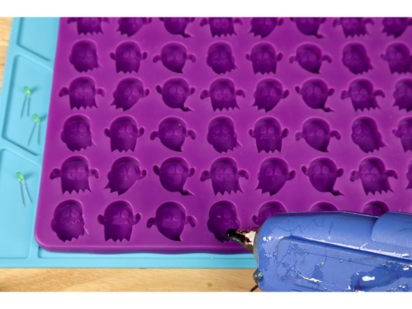 Plug your hot glue gun in and load a glue stick of choice. When the glue is hot enough to flow, squeeze a small amount into your mold cavity near what will be the bottom of the object when you pop it out of the mold as shown in photo 1 and 2.