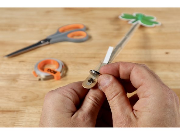 Stick that tape loop to the end of the smaller Maker Tape section located on the switch side one the wand handle. Then stick the battery on top of the tape loop Positive (+) Side facing UP. The dimpled Negative (-) Side of the battery is now in contact with the path that leads back up to the Negative (-) LED Leg.