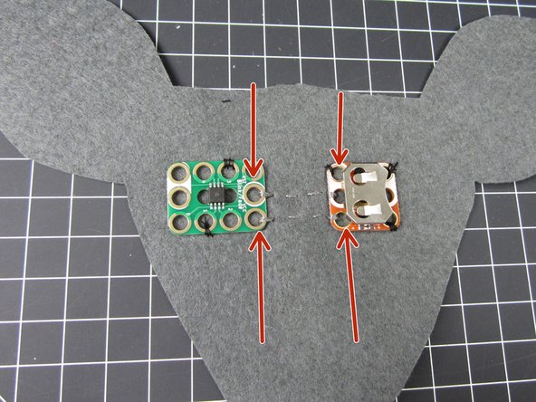 Using Conductive Thread, connect the orange colored hole on the Battery Holder to the VCC Hole no the Blink/ Fade Board.