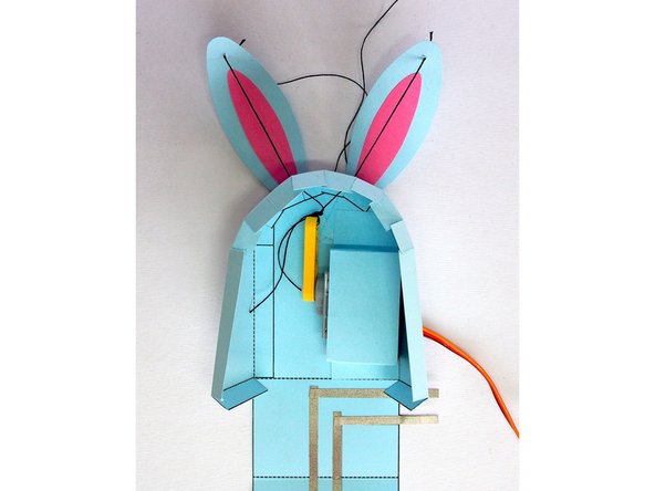 You want to tie it so that when the LEGO axle mount points up, the thread is loose enough for the ears to be fully extended, but when it points down, the thread is tight enough to pull the ears down