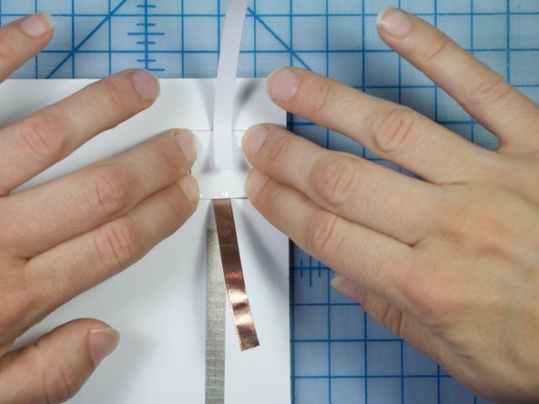 With the cardstock piece placed in the square and the flaps folded down so that only a small amount of the Maker Tape inside is visible, place the square piece in the square hole face down as shown.