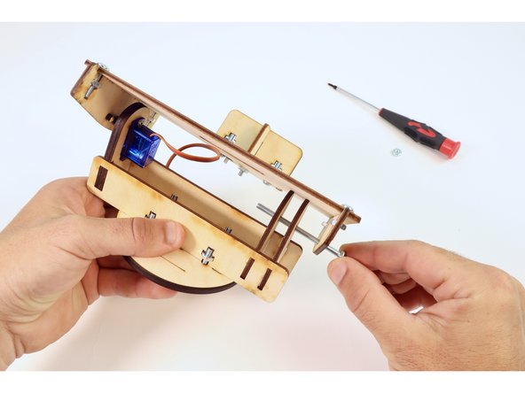 Locate the longest screw in your kit and thread it through all three holes in the wooden pieces on the opposite side of the servo connection you just made.