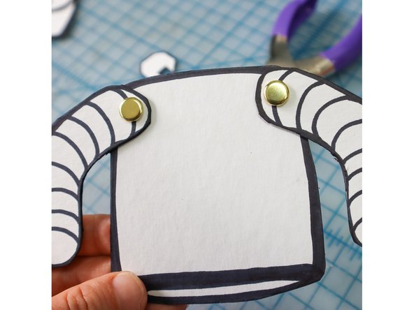 Insert the Paper Fastener through the holes in the arms and then the body. Flatten the legs on the other side making sure that they don't go over the edge.