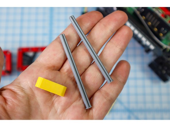 Insert the axles with flat ends into the outer holes of the yellow beam, and thread on the other components as shown: full red bushings, and small gears.