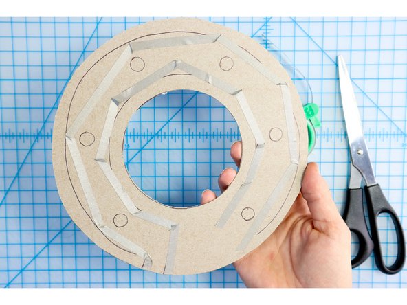 Stick two paths of maker tape to the cardboard. One will start on the back and go around the outside of the LED markers. The other will start about one inch from the first (also on the back) and go around the inside of the LED markers as shown.