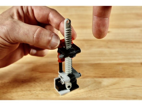Guide the top of the gear rack through the space behind the bevel gear of the latest build and then seat the axle holes into the tops of the two tall axles. Slide this portion down the axles until they meet the rest of the cross blocks below.