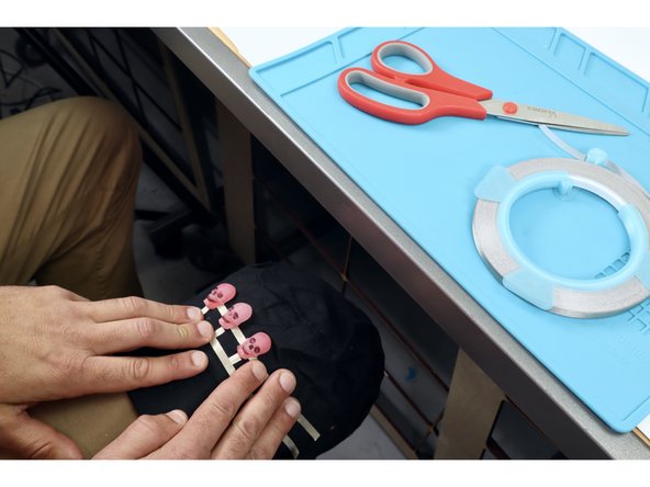 Now, peel the connected LED array carefully off the table and transferring it to the front area of the hat. You can either a) simply press/stick it atop  the hat OR, for a firmer mount on some fabrics b) flip the connected arrangement over, apply a layer of hot glue to the back of paths and LEDs/then stick.