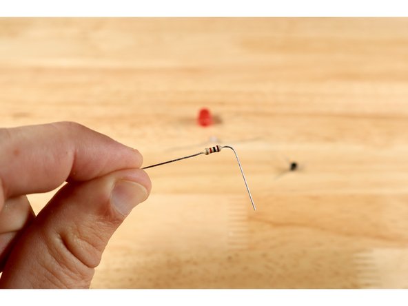 Using the flat side of the 3 legged transistor as a guide for orientation, bend the three legs outward away from the center of the part as shown on the template. This should allow for the part to be placed as shown with the flat side of the black part facing the bottom of the template; two legs extending outward and the middle one extending upward.