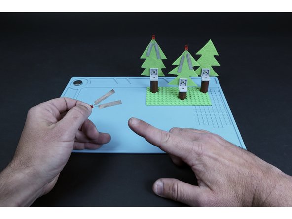 Taking care to orient the LED legs as shown on the guide, peel and stick a piece of Maker Tape over each leg  and then TO  the backside of the felt. Make sure to bend the legs outward slightly so that the two tape paths  do not touch one another.