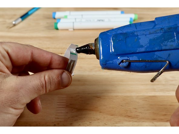 Use a hot glue gun to put a dab of hot glue on the band and glue the two halves of the band together at the point you marked. Once the glue has cooled, you can put the ring back on and finish shaping it.