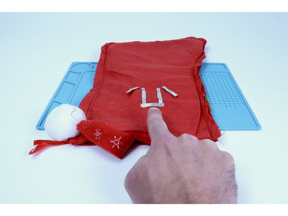 Cut a small piece of Maker Tape that is long enough to span the distance between those two shorter legs. Peel and stick it as shown, connecting those two shorter LED leg pathways.