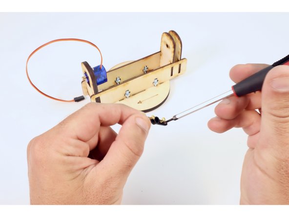 Find two of the four gold screws included in your kit. On a flat surface away from the wooden assembly, screw one into the hole second from the center of the servo horn and the other  into the third hole from center on the opposite side of the center.