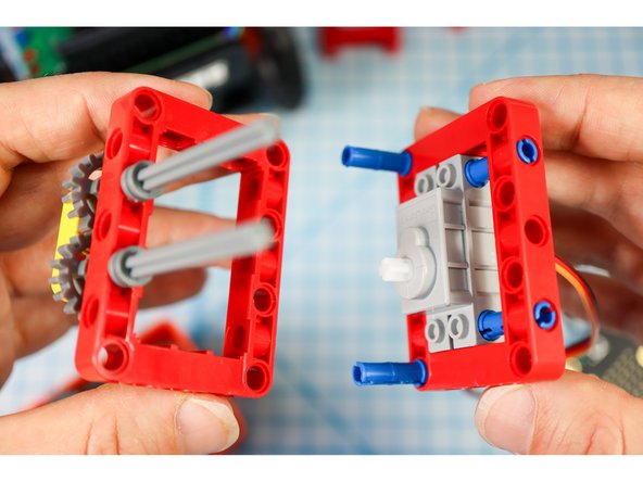Get the frame piece with the motor attached and connect the two together as shown, with the blue pins on the bottom and the gray axles on the top.