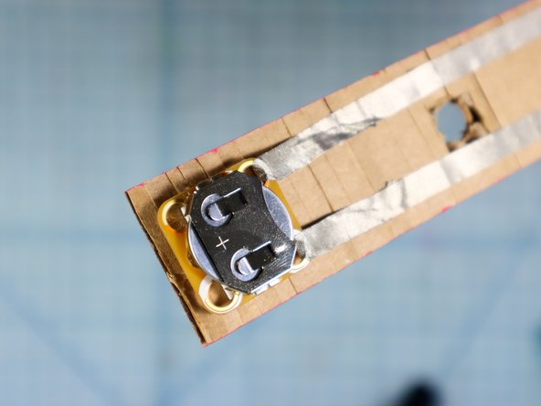 Use a piece of foam mounting tape to place the battery pack at the end of the belt. Double-check that the positive hole will touch one of the rails of tape, and the negative hole will touch the other.