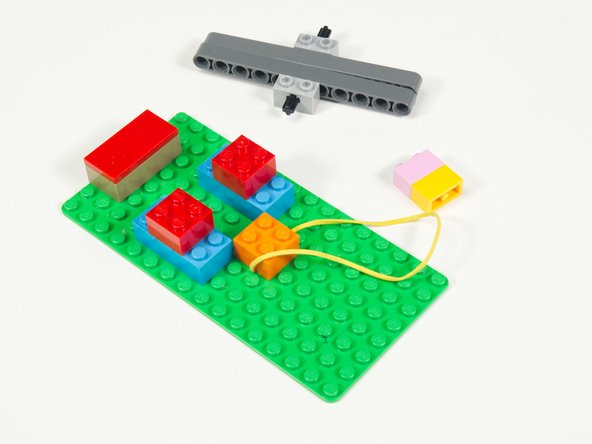 Place the rubber band under the brick and then stick the brick down to the baseplate.