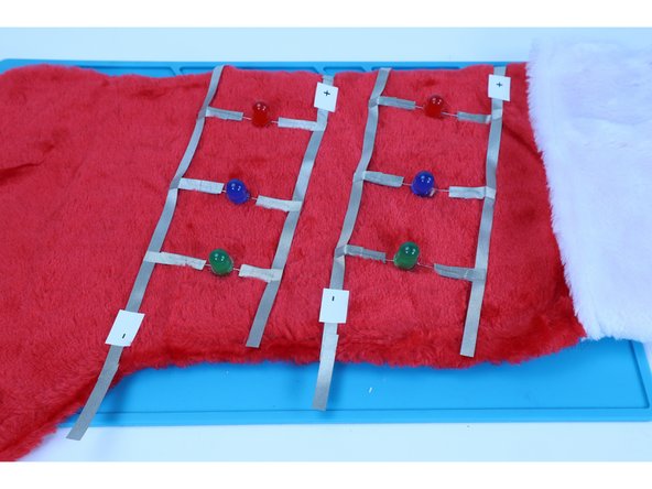 Recall that the paths on the back are electrically connected to the voltage source (your AA battery pack). Also recall that now all your LEDs are electrically connected to two separate   (2) path arrangements on the front. The front and back, however, are NOT connected. 