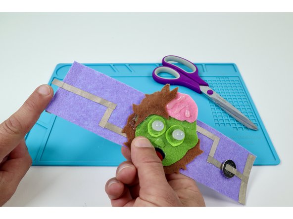 To finish this side of your circuit and connect to the remaining edge pad on the opposite side of the bracelet, measure and cut one final Maker Tape path that goes from the current end of this side to a point just past the edge. 