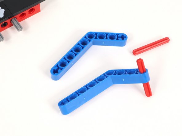 Insert a 4 stud long red axle into the plus-shaped hole at the end of the short side of a blue bent beam. You will need two of these.