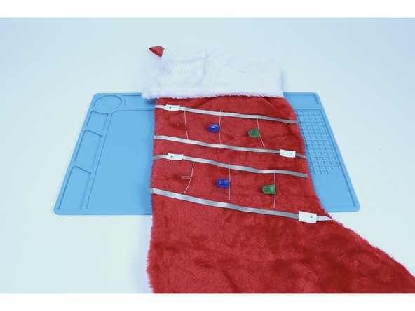 Bend the legs of your LEDs in opposite directions so that they can lay flat against the stocking fabric. Note that each LED has a long leg and a short leg. Lay them out as pictured so that the long legs are oriented toward the Maker Tape paths you labeled (+) and the short legs are oriented toward the paths labeled (-).