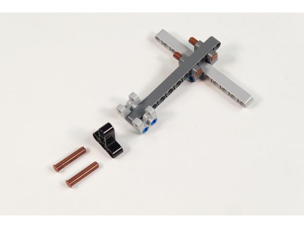 Place 2 LEGO Axle 4 with End Stop  halfway through LEGO Beam 3 x 3 T-Shaped as shown.