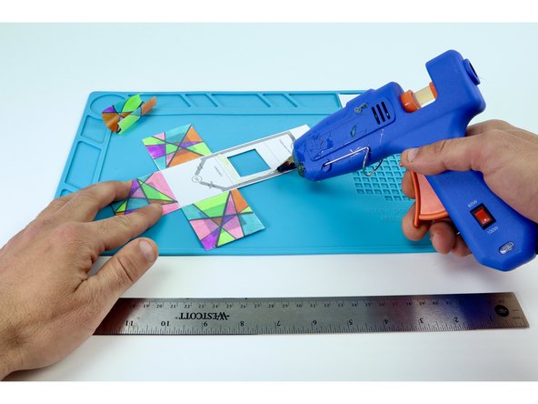 Use a hot glue gun to place hot glue on the inside of a frame while pressing one of the colored squares into place on top. Be sure to be accurate with your placement as each edge of a given face will eventually need to be fastened to the next. Overhang can make this tricky.  Do this ONE FACE AT A TIME. 