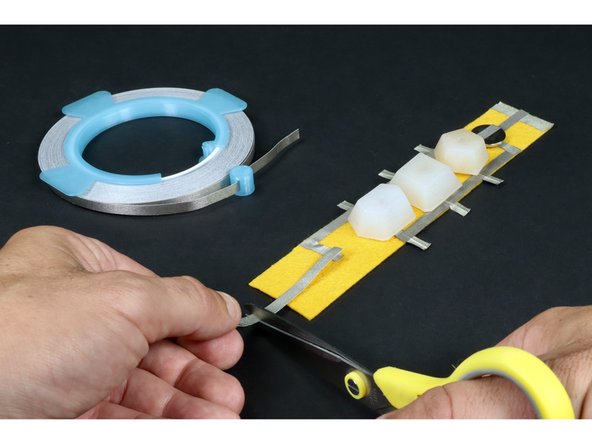 Measure, cut, peel and stick another small piece of Maker Tape that connects to the end  of the path that connects all of the long LED legs and reaches to the middle of the felt. When done correctly, it should look like photo 2.