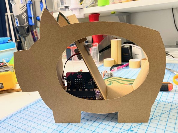 We used hot glue on the outside of the box between the two pig silhouettes because we would be covering it later with other cardboard (so you won't see it in the end). Hot glue is quicker than superglue (but looks a bit messy).