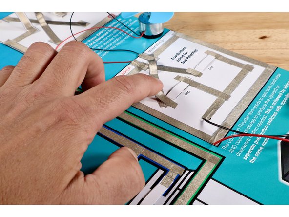 Peel and stick the Maker Tape pieces atop the switches to secure them in place as shown. The switches should have slight upward bend to them so that the conductive surface underneath is not normally in contact with the path ends/gap below.