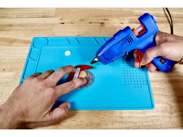 Using a hot glue gun and photo one for reference, squeeze a small dot of hot glue atop the tip of the hat that hangs down.