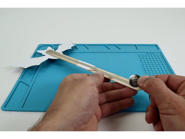 Begin the battery installation by sticking the CR2032 battery atop the tape loop with the positive (+) side facing UP.