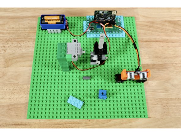 The battery pack, distance sensor, and servo all have cables that will need to connect to pins on the Bit Board. Lay the parts and their mounting builds out first so that they aren't too far for the cables to reach the pin areas on the Bit Board. Leave adequate space immediately adjacent to the servo axle for the gear rack build as well.