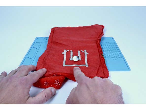 Cut a new piece of Maker Tape that is long enough to span the distance between those two longer leg pathways. Peel and stick it as shown, connecting those two longer LED legs.