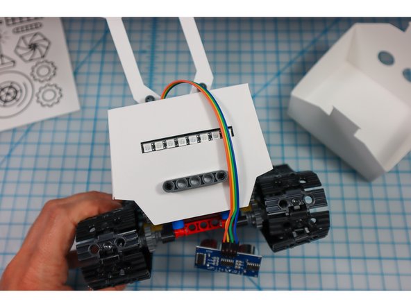 Place the paper body over the bot (hint: put the arms up and thread the Distance Sensor through the hole before wrapping it around.