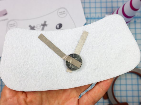 Add a small loop of Maker Tape with the adhesive side out on the negative side of the battery, then place it on top of the Maker Tape.