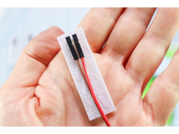 Use hot glue to glue two jumper wires to the back of each rectangle as shown. Make sure the hot glue doesn't cover the ends of the wires.