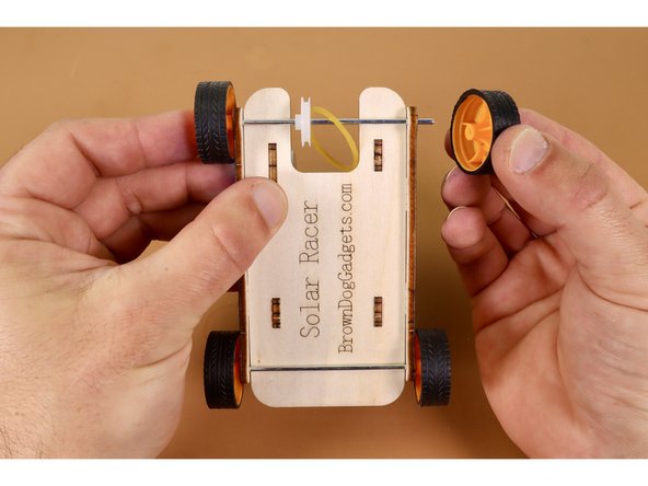 With white axle wheel and rubber band in place, continue threading the end of the axle rod through the final hole and press the remaining wheel onto it afterward.