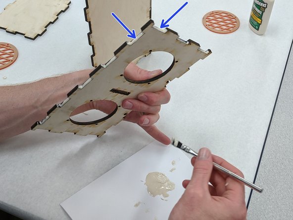 (4)Locate the front of the box, the piece with the large circular holes.  Apply glue to the inside of the teeth along the bottom edge (opposite the T-slots) and to the inside of the teeth along one of the two short sides.