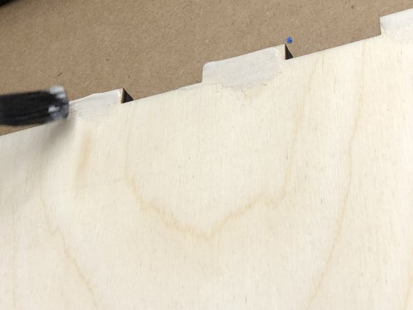 Starting with the bottom, paint wood glue onto the interior of the teeth of one of the short ends of the box.