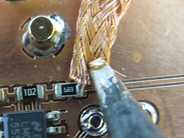 The idea is to sandwich the copper braid between the solder bridge and the iron.  The soldering iron will heat up the braid  and solder, the solder will melt and wick onto the copper braid, and then the braid can be removed along with the solder bridge.