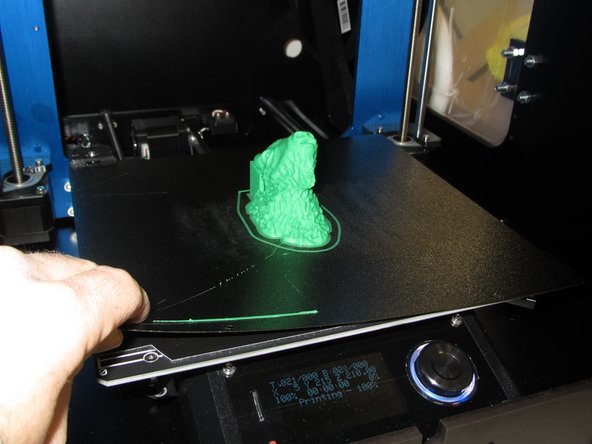 When your print completes the print head will move to the top of the printer and the print bed will move forwards.  Gently lift up on the metallic print surface to completely remove it from the magnetic base.