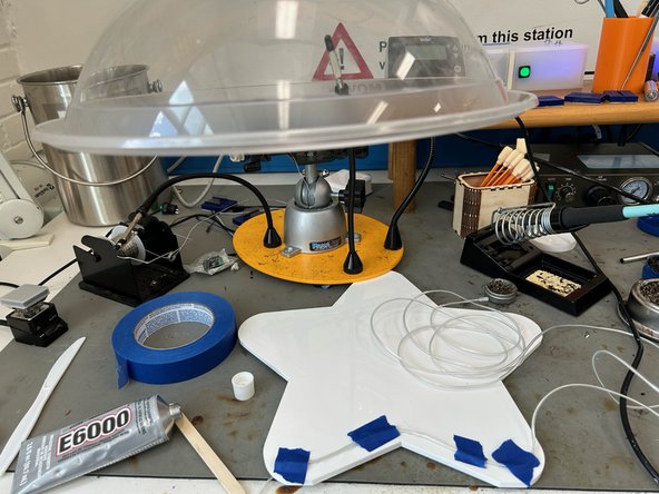 Make a small line of glue where the wire will go. Lay the wire down on top of the glue. Take a small piece of tape and tape the wire down over the glue. Repeat this for the rest of the sign.