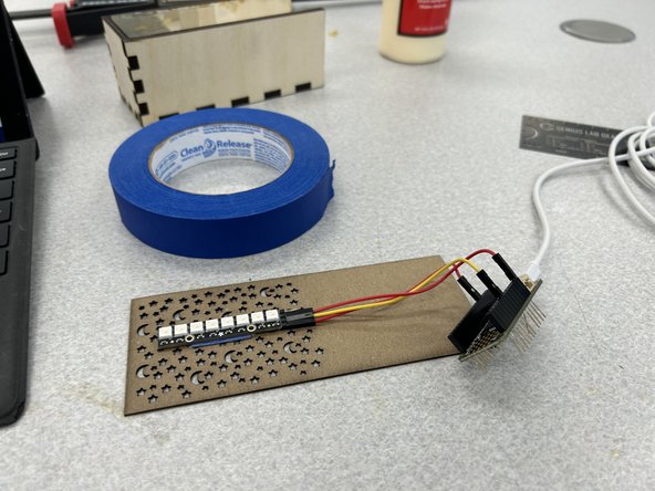 Make a tape loop using any tape.  Tape the Neopixel onto the top of the lid as shown, making sure the wired end is towards the blank end of the cardboard.