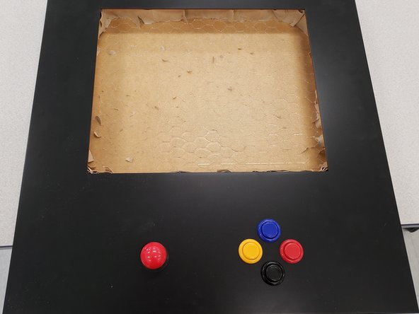 Remove the black washer and the red ball from the joystick. Underneath the table, move the joystick to the location indicated by the laser-cut holes. Screw the red ball and black washer onto the above-table portion of the joystick.