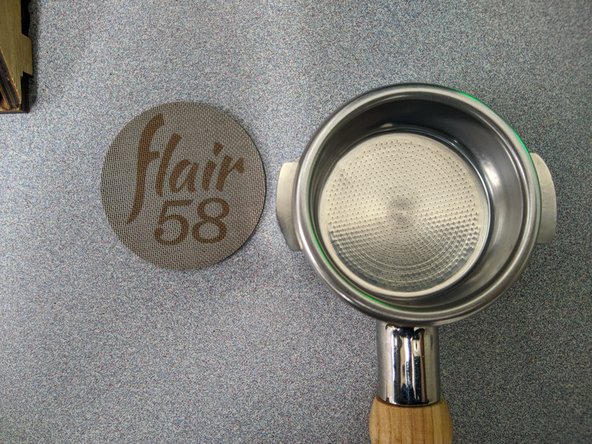 Remove the warm portafilter from the brew chamber of the Flair press.  Grab the wooden handle and rotate it left to 6 o'clock to remove it.  Be sure to remove the puck screen from the brew basket and set the screen aside for after grinding.