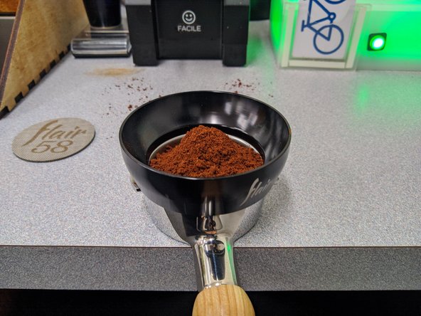 Place the magnetic black funnel on the portafilter.  Shake the portalfilter from side to side to help distribute the grounds.  Firmly tap the portafilter on the counter to help the grounds settle.  The funnel should help prevent the grounds from falling out of the basket.