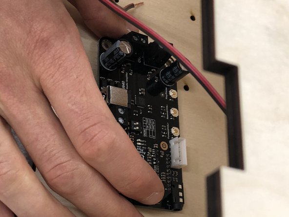 The amplifier board goes inside the speaker box on the back surface's left hand side as you are facing the front of the box.