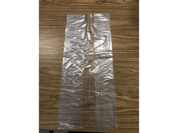 Lay plastic bag flat on table. Bag must be well sealed, wide enough to loosely fit PAPR and long enough to reach shoulders. Sealed end of bag is top. Polyethylene &quot;kick bucket&quot; liners are nearly perfect size and strength..