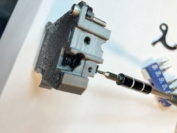 Attach optical interruptor rod to sensor lever. Its end has a shallow wedge shape to help with alignment. Rear of extruder body has opening through which a finger can support the lever