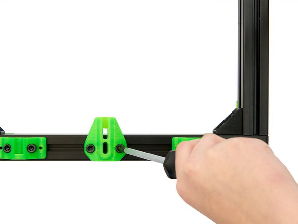 Setzen Sie den y-Riemenspanner auf 2x Nutensteine in der vorderen x-Achse und befestigen Sie diesen lose mit 2x M6x12mm Zylinderkopfschrauben.