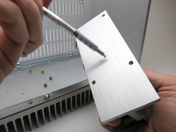 Peel the label from the syringe of thermal paste so you can monitor the volume.  Empty 1/2 contents of the syringe onto each T-bracket.